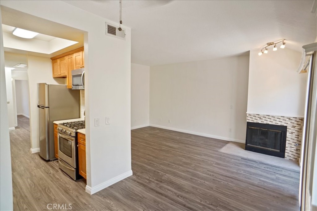 Unfurnished living room with gray wood-look flooring, tiled fireplace, and adjoining kitchen.