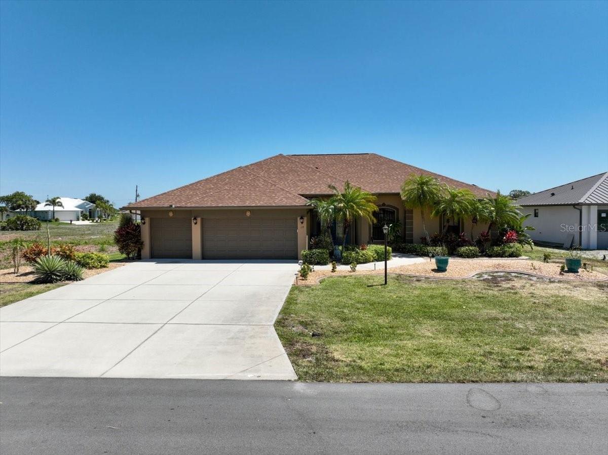 Single-story tan home with a two-car garage, curved driveway, and palm trees in the front yard.