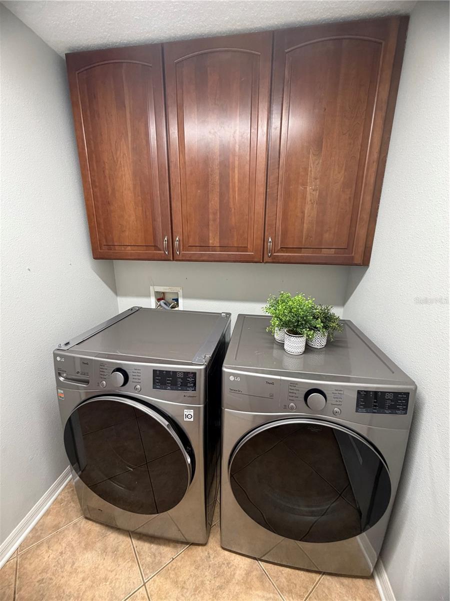 Laundry room with matching front-load washer and dryer beneath dark wood cabinets.
