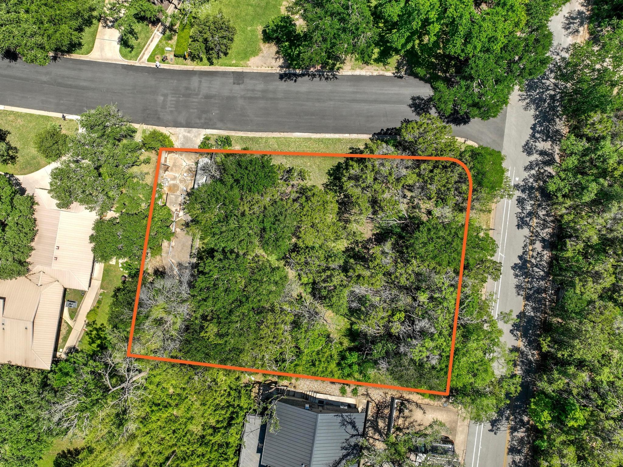 Aerial view of a wooded vacant lot outlined in orange between two residential streets.