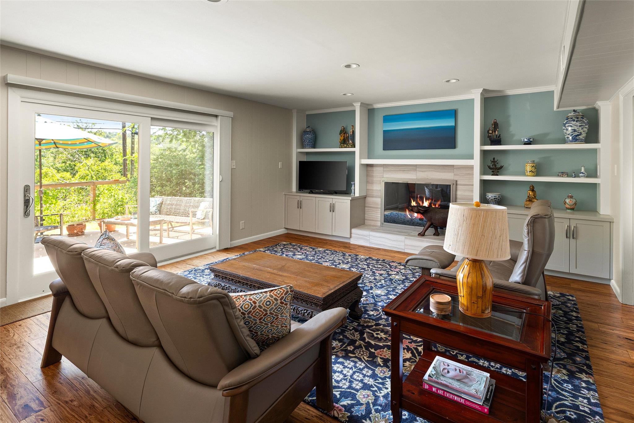Living room with a lit fireplace, built-in shelves, and sliding doors opening to a sunny deck.
