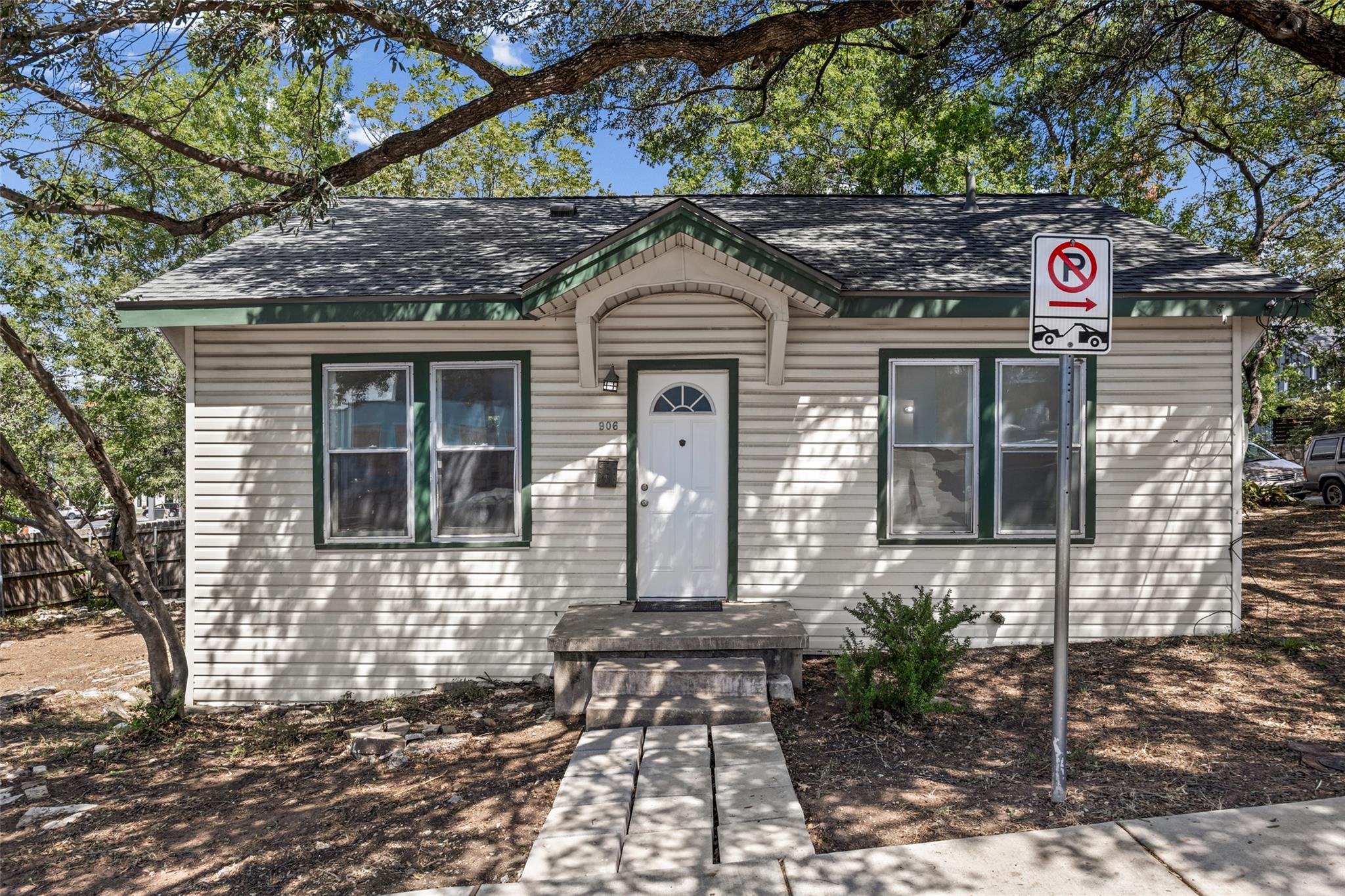 Small white-sided home with green trim, a gabled entry, and mature trees overhead.