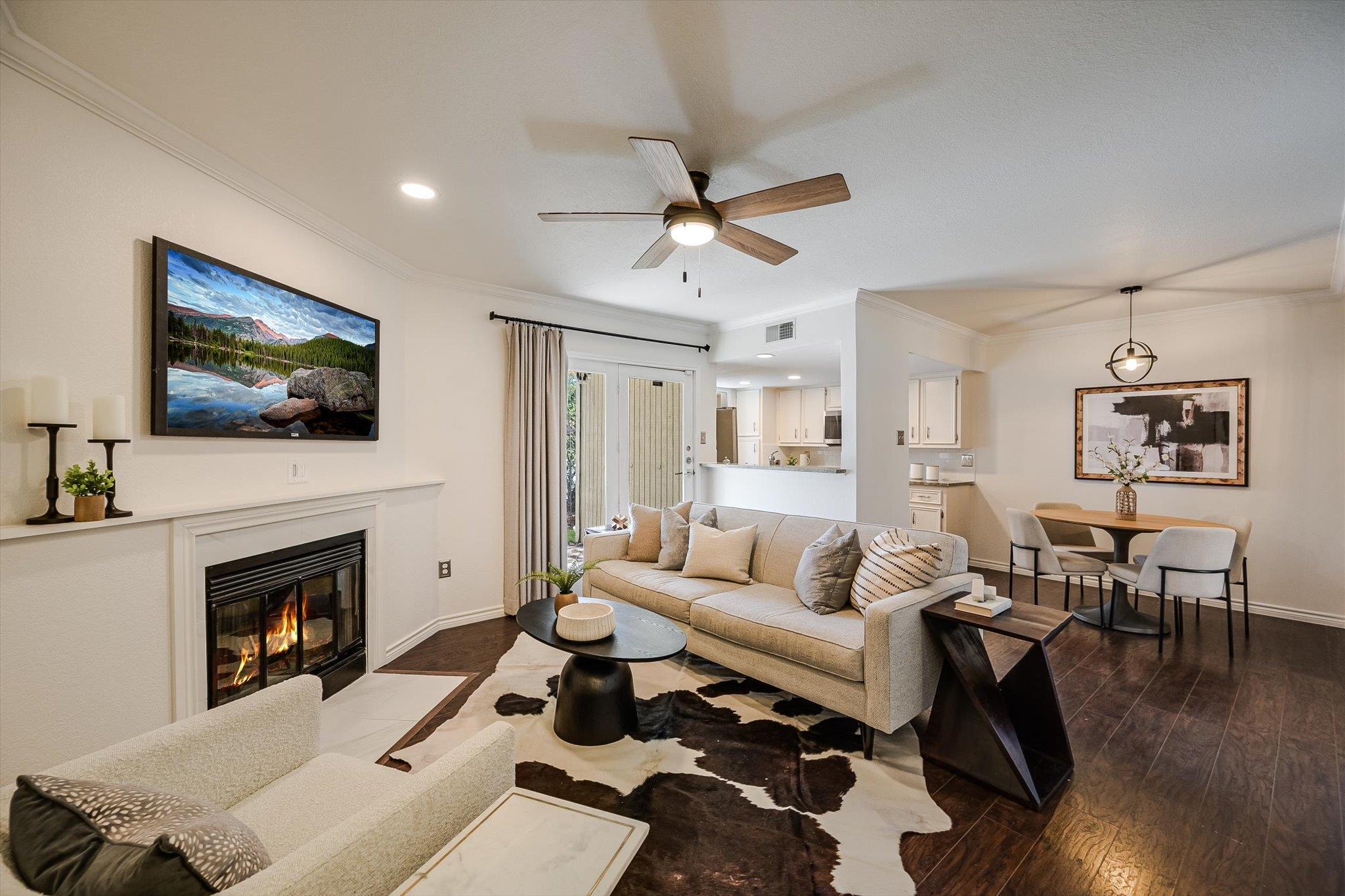 Staged living room with a fireplace, ceiling fan, and adjoining dining area and kitchen.