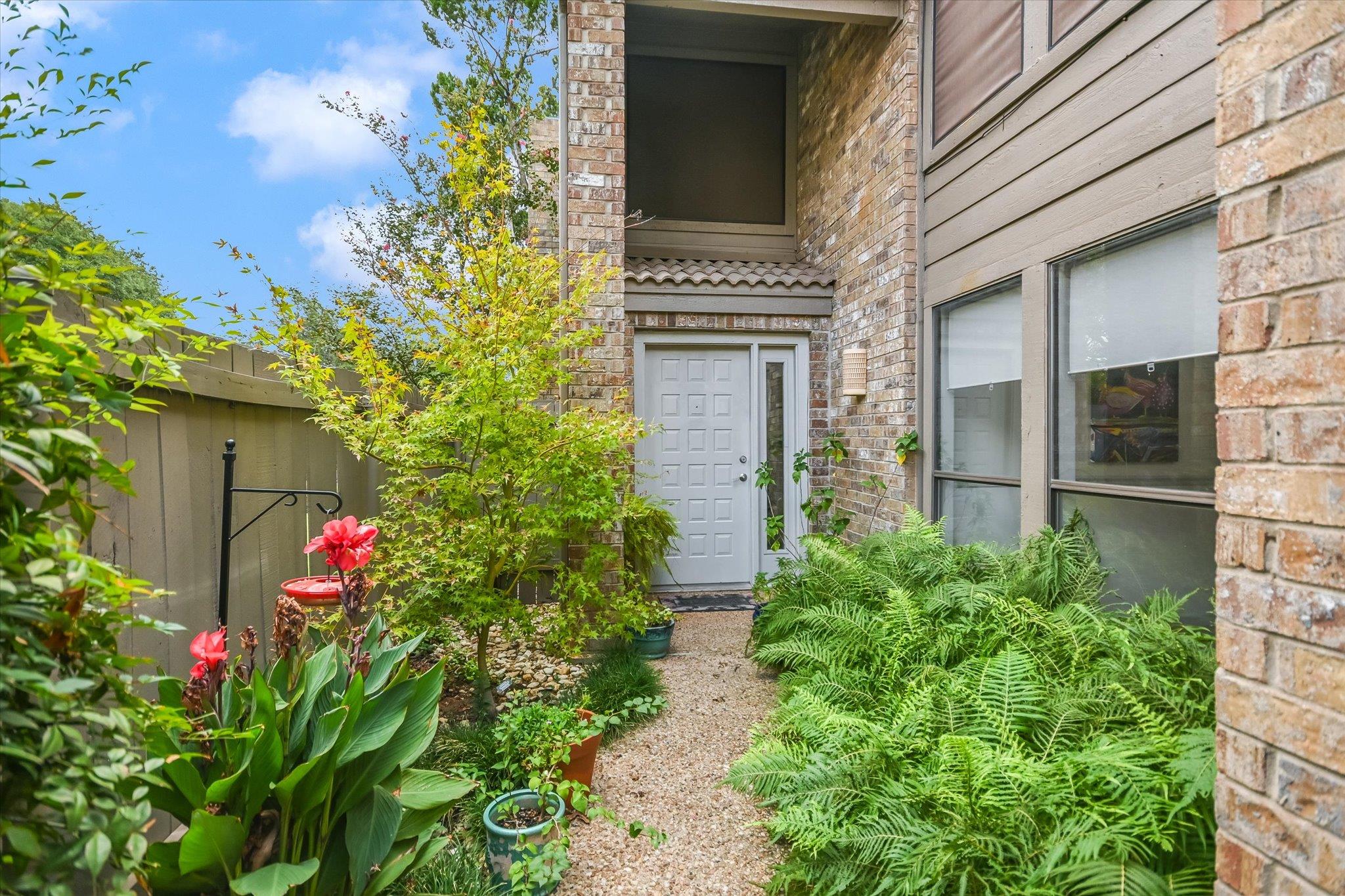 Home entrance with a white door, gravel path, lush ferns, and flowering plants.