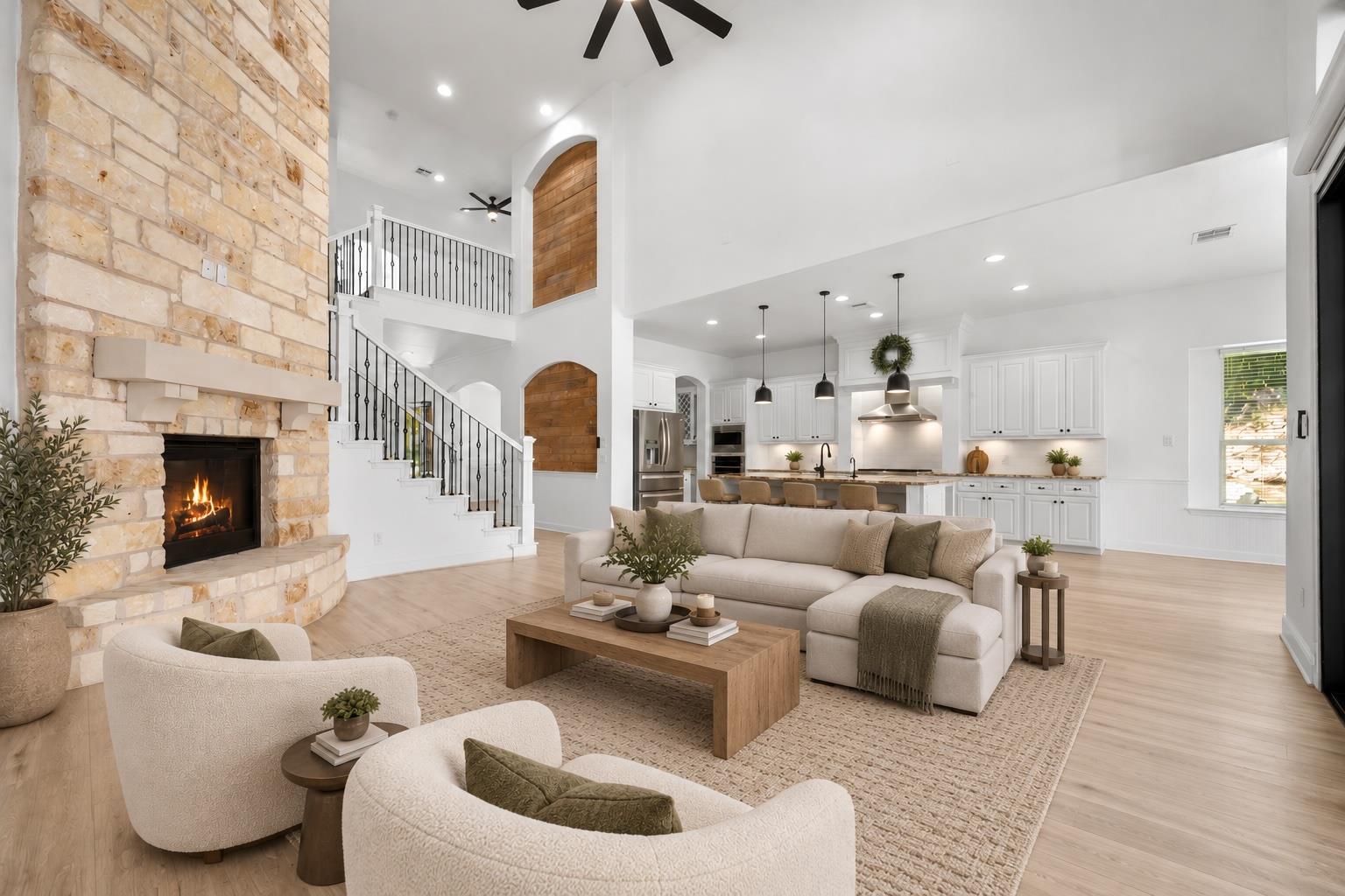 Open-plan living room with a stone fireplace, white kitchen, and iron-railed staircase.