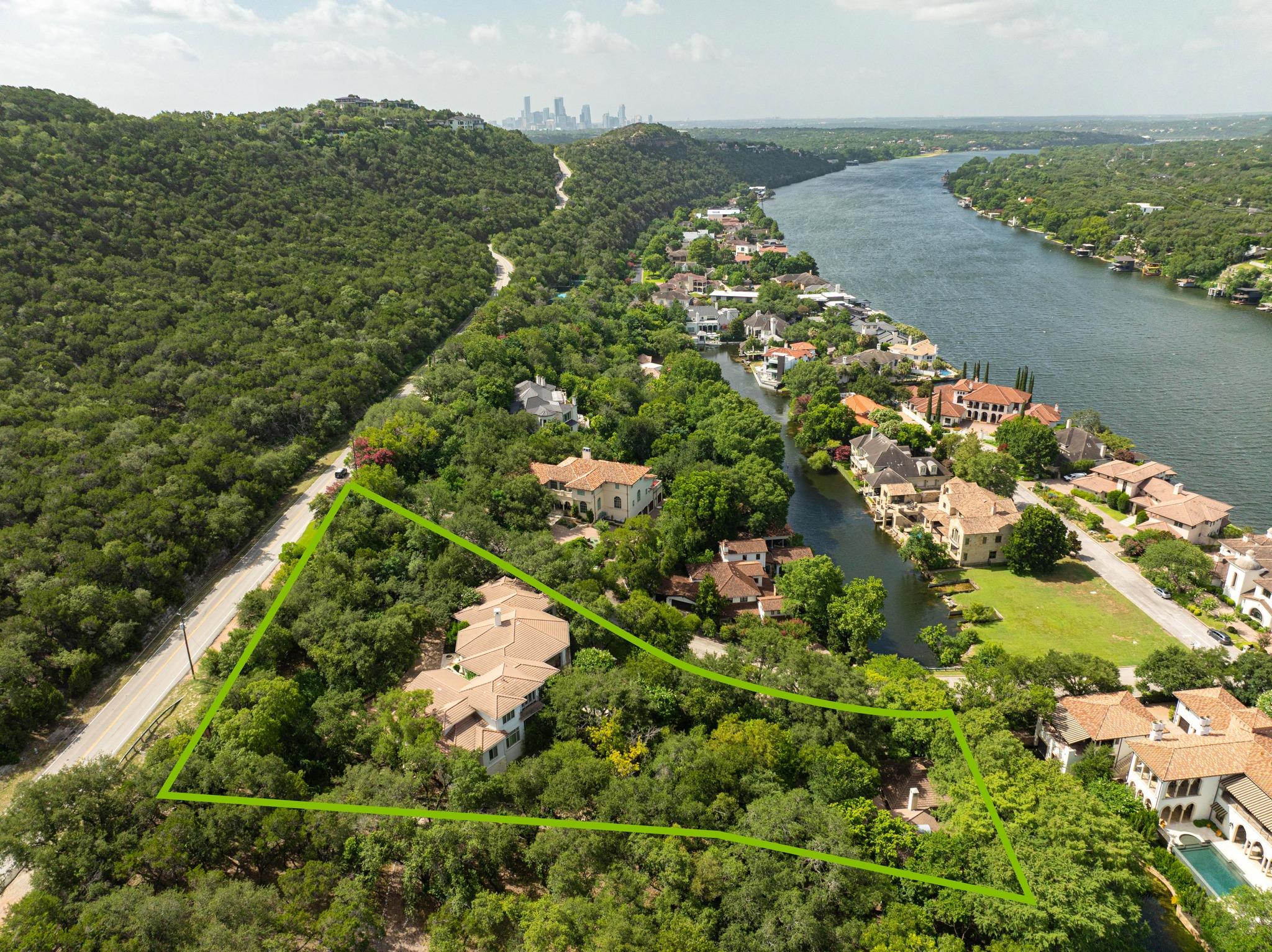 Aerial view of a wooded property outlined in green beside a river, with the city skyline in the distance.