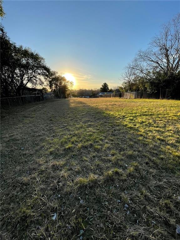 Grassy vacant lot bordered by wooden fences and mature trees in the evening sun.