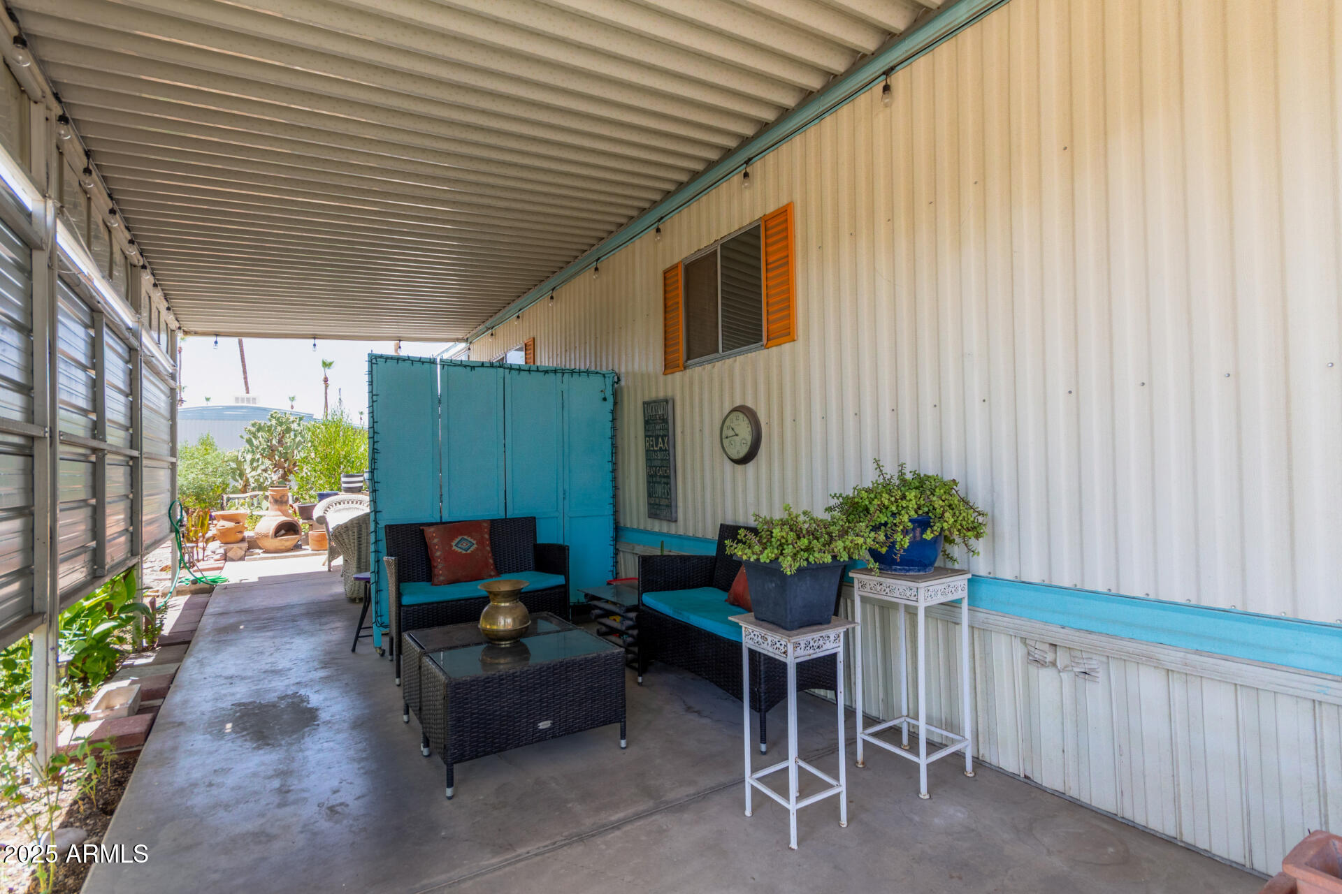 Covered patio with wicker seating, turquoise privacy screens, orange shutters, and potted plants.