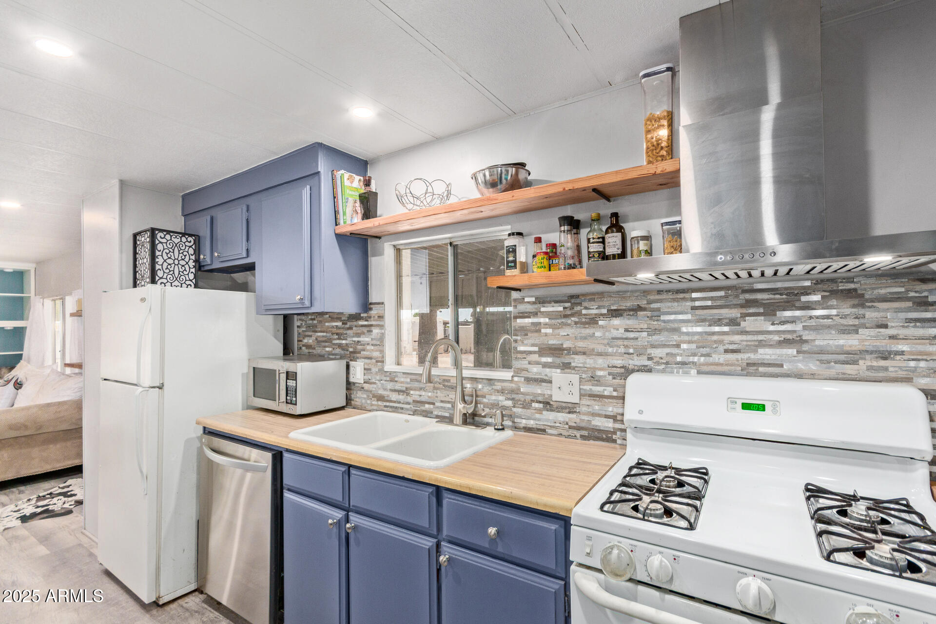 Kitchen with blue cabinets, wood countertops, open shelves, and a stainless steel range hood.