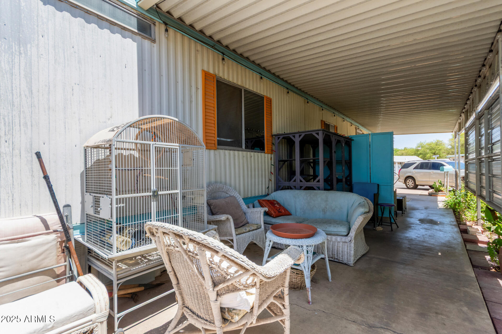 Covered patio with white wicker seating and blue storage cabinets beside the home.