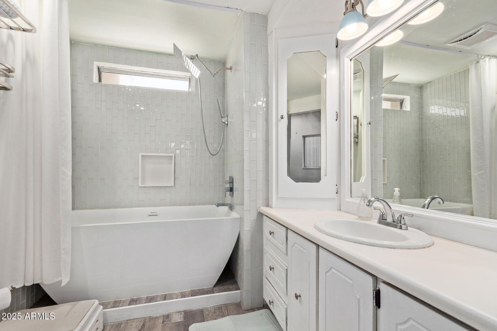 Bathroom with a white tub, pale gray tile, and a long vanity beneath a large mirror.