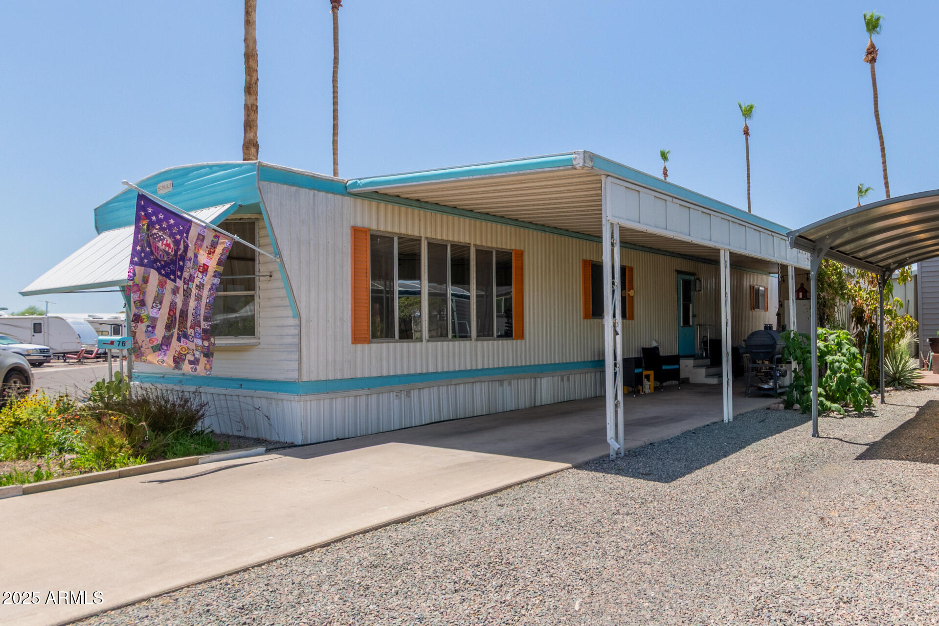 Manufactured home with turquoise trim, orange shutters, and a covered carport.