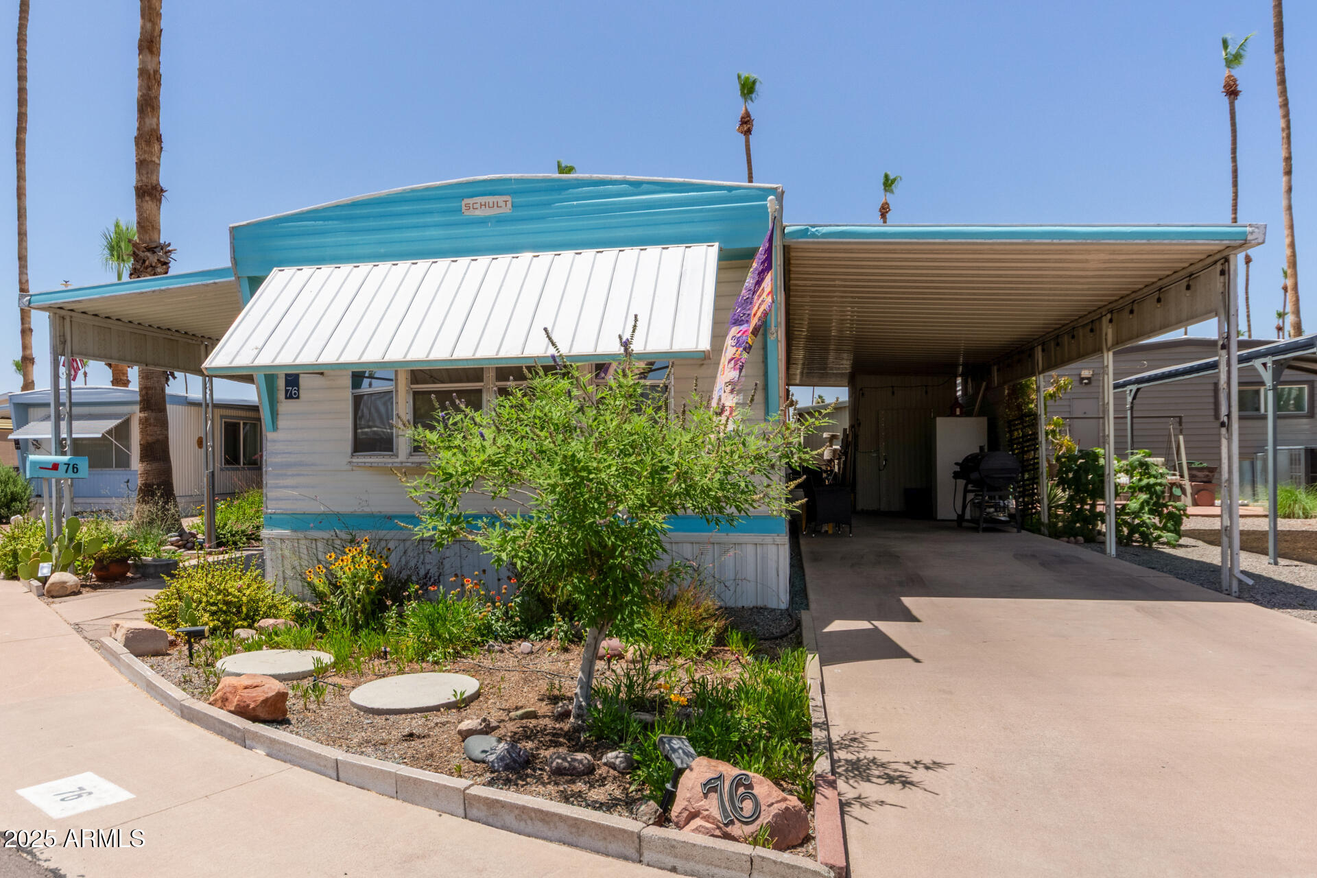 Turquoise-and-white manufactured home with a covered carport and landscaped front yard.