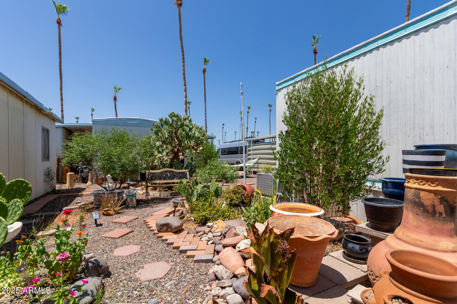 Landscaped courtyard with gravel paths, desert plants, and large decorative pots between manufactured homes.