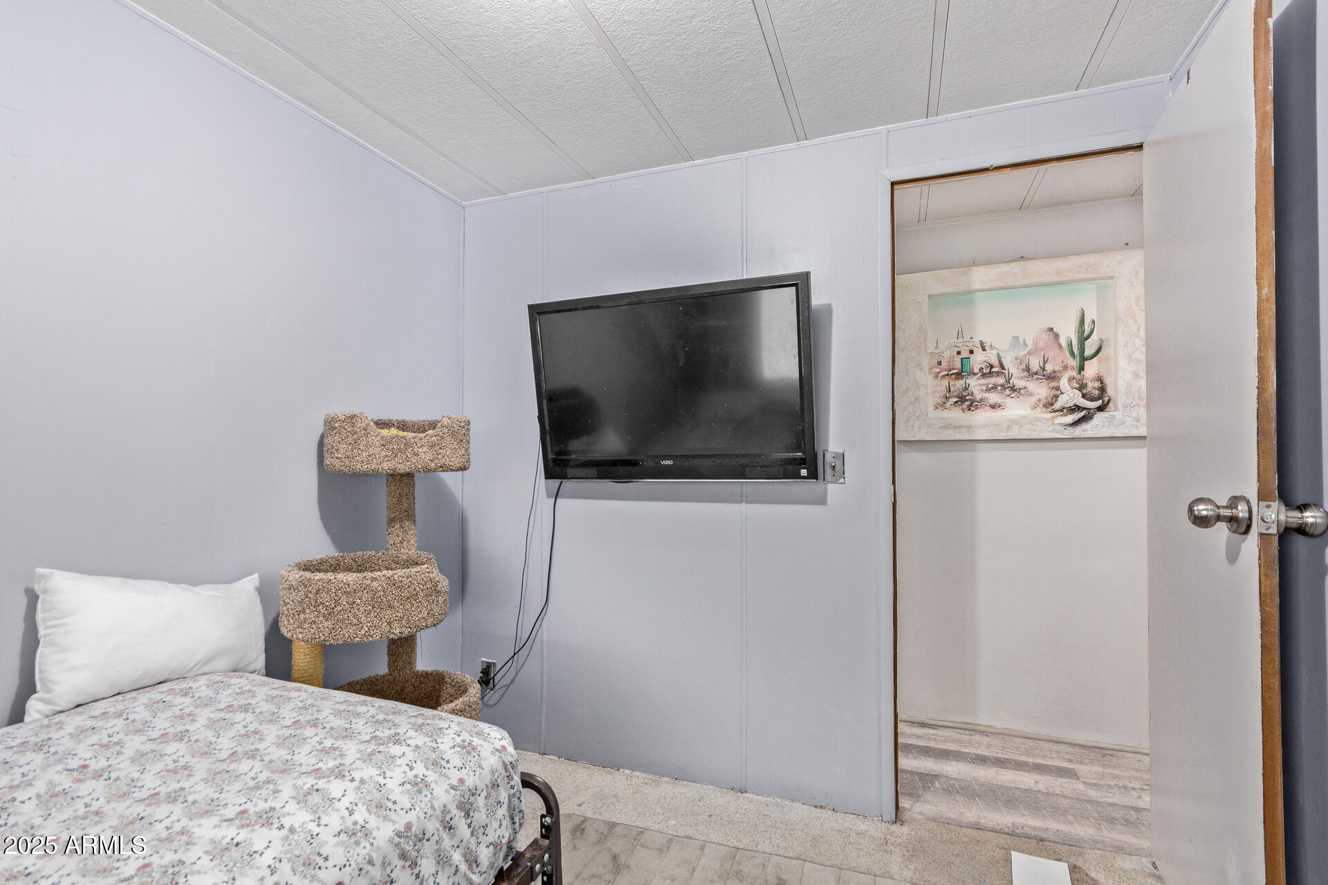 Bedroom with a bed, wall-mounted television, and carpeted cat tree beside an open doorway.