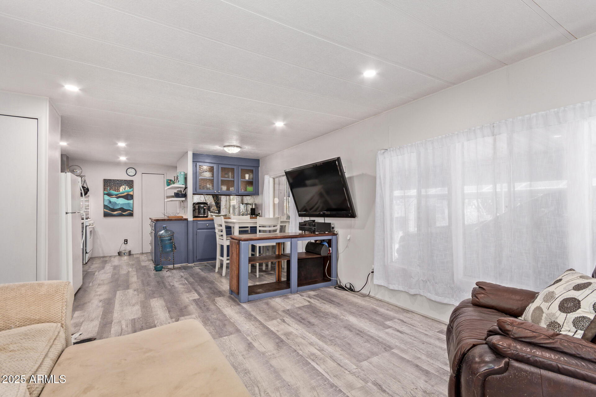Living room with blue kitchen cabinets, gray plank flooring, and a wall-mounted television.