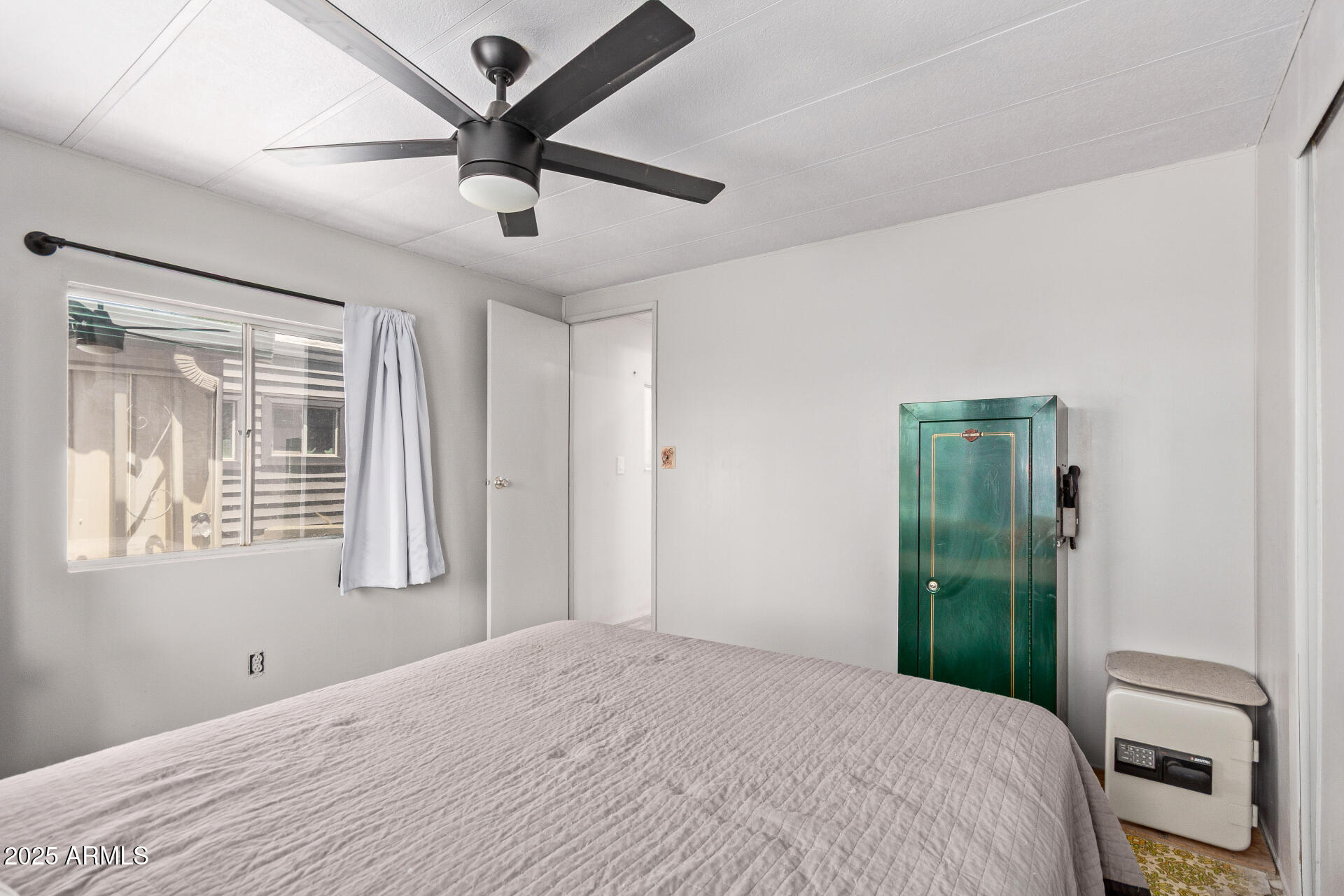 Bedroom with a gray bedspread, black ceiling fan, and distinctive green cabinet.