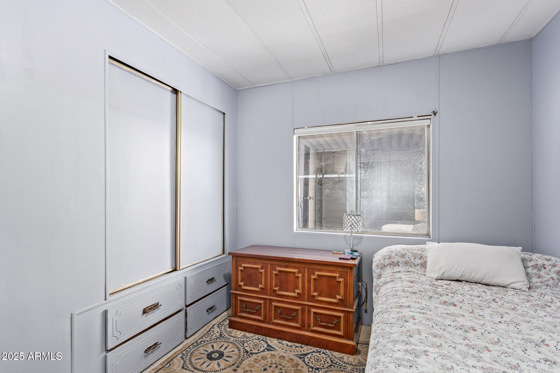 Bedroom with floral bedding, built-in drawers, and a wooden dresser beneath the window.