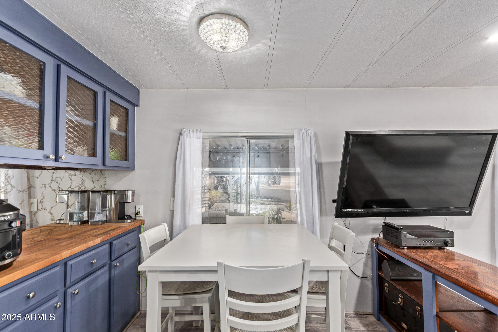 Dining area with a white table, blue cabinetry, wood countertops, and a large wall-mounted television.