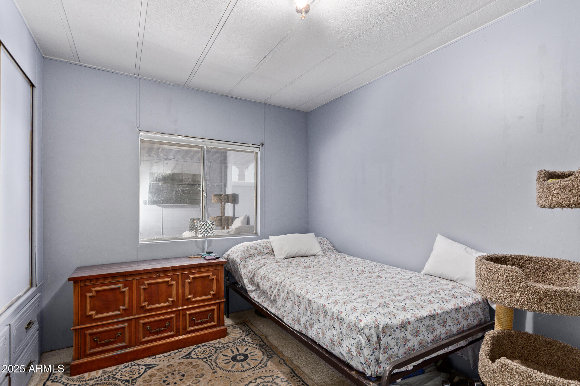 Bedroom with a floral-covered twin bed, wooden dresser, and carpeted cat tree.