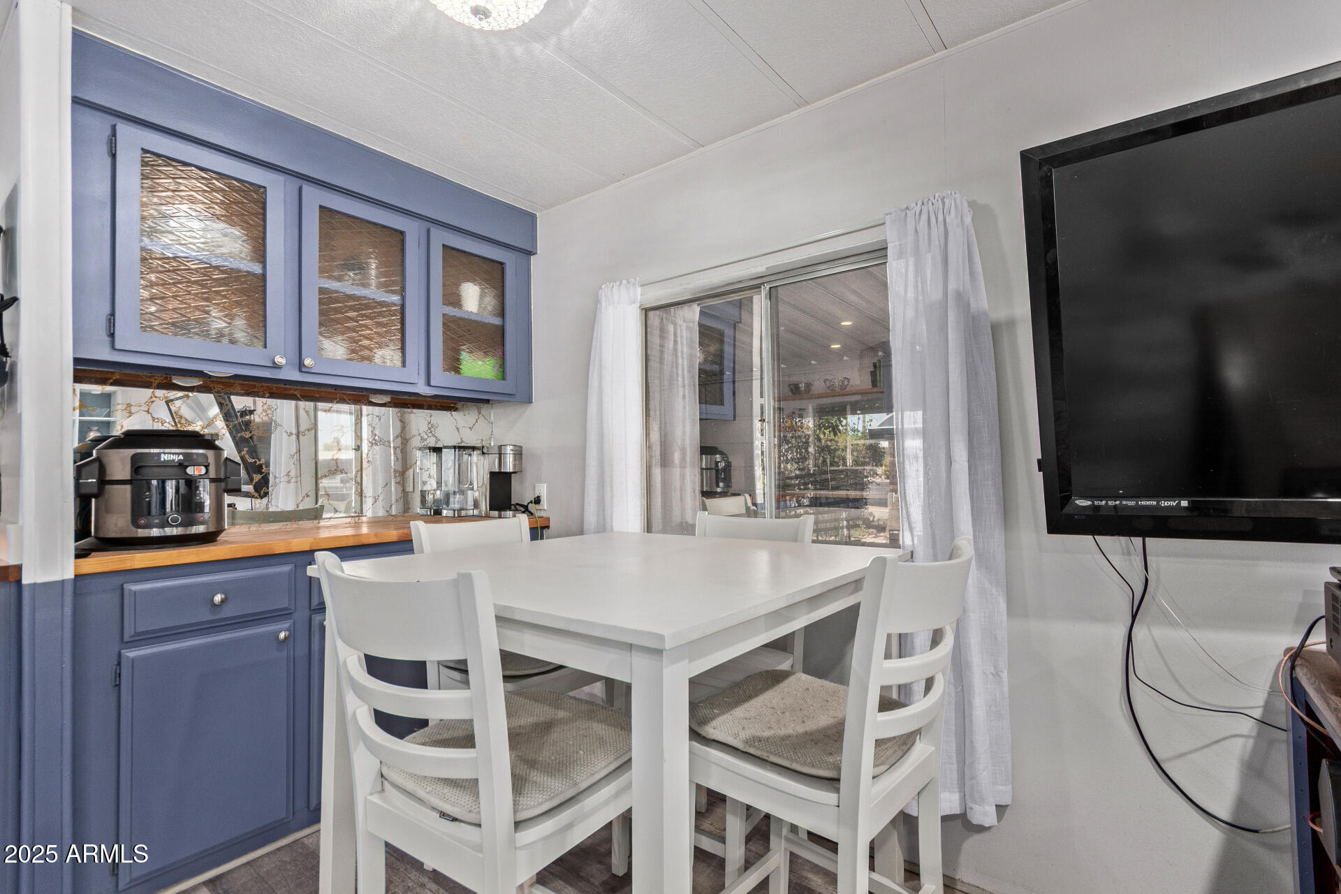 Dining area with blue cabinets, a white table and chairs, and a sliding glass door.