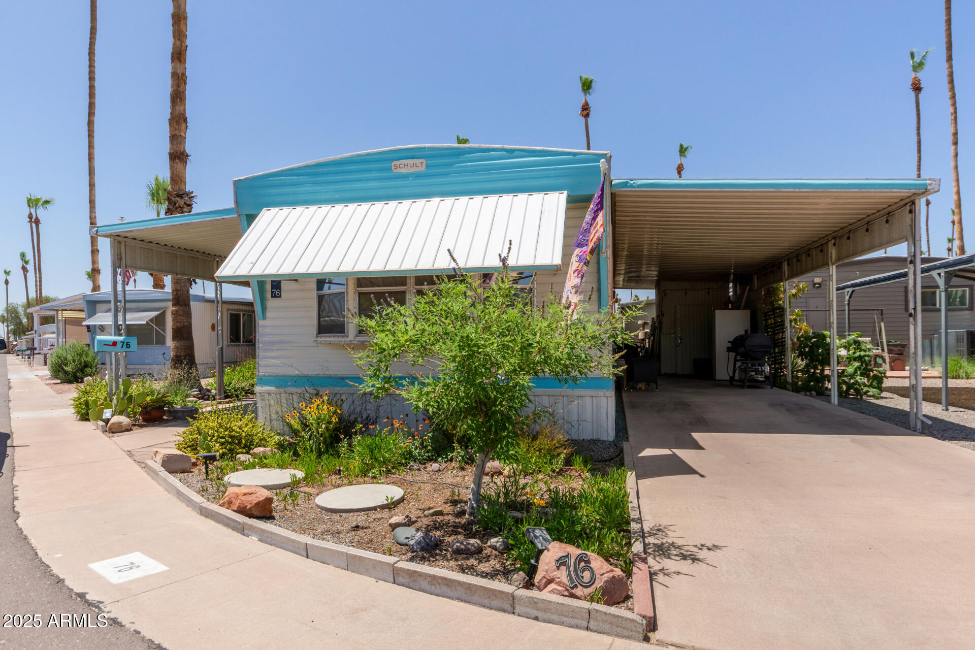 Manufactured home with blue trim, a landscaped front garden, and a large covered carport.