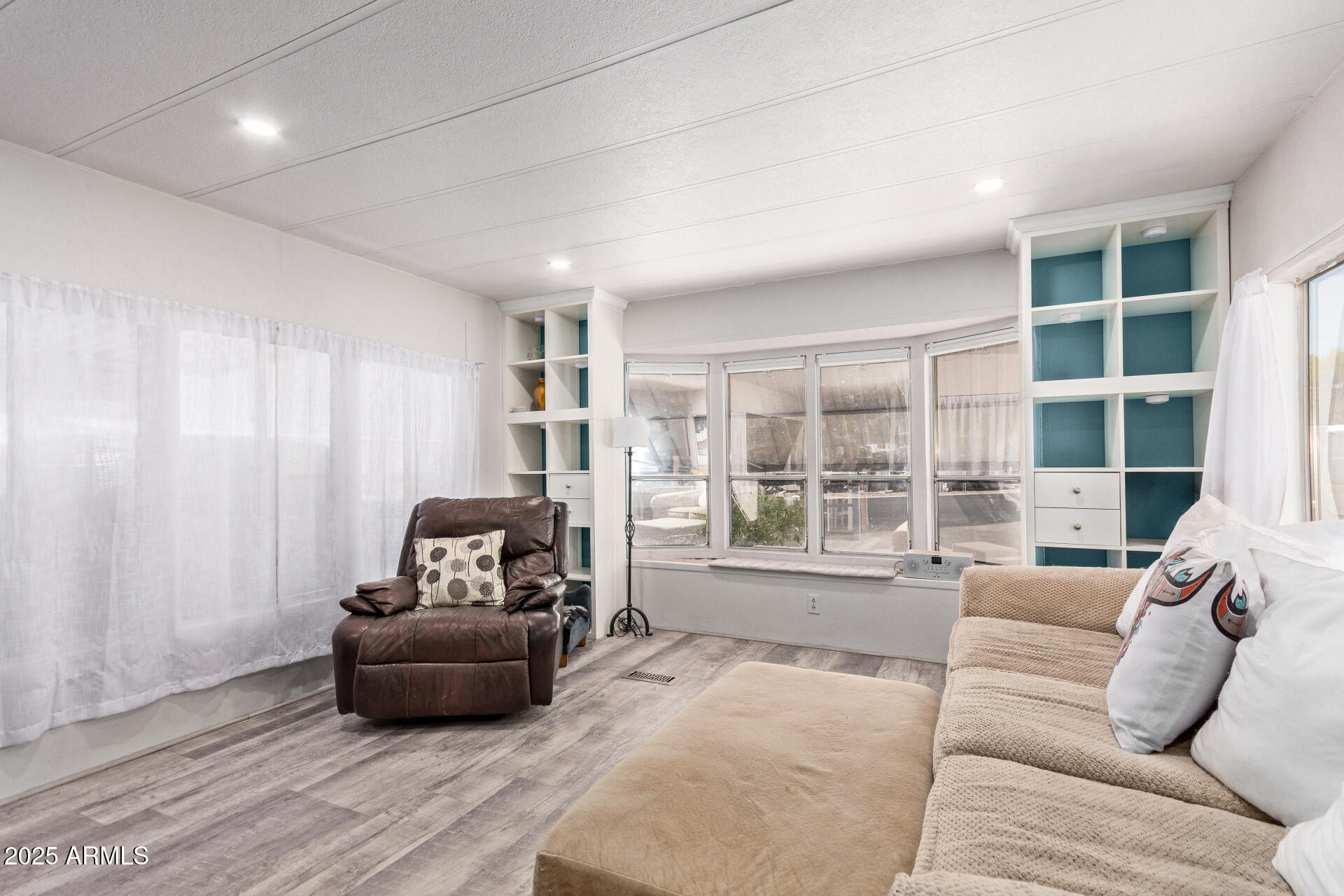 Living room with a leather recliner, beige sofa, large windows, and teal-backed built-in shelves.