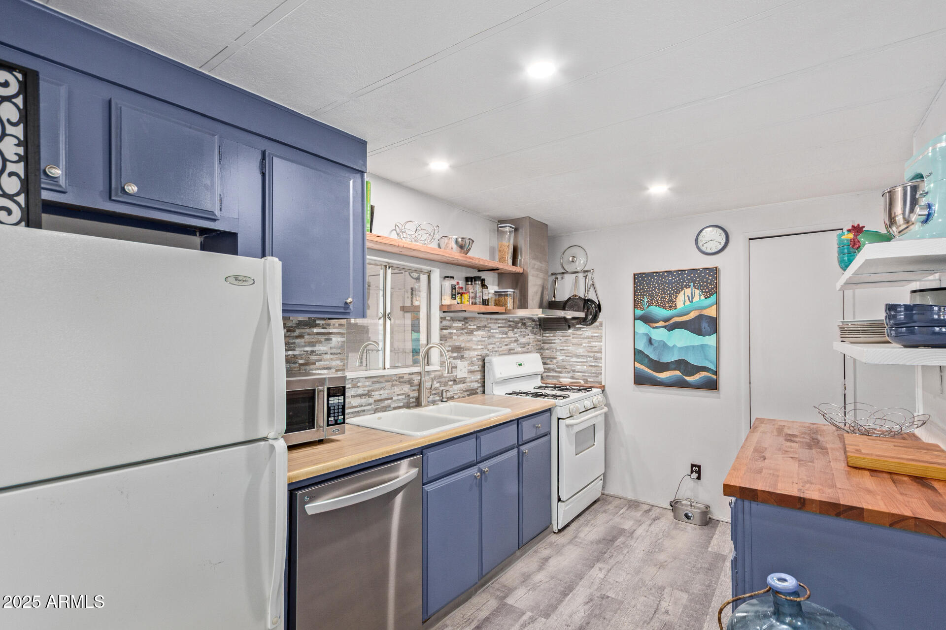 Kitchen with blue cabinets, wood countertops, gray tile backsplash, and a butcher-block island.