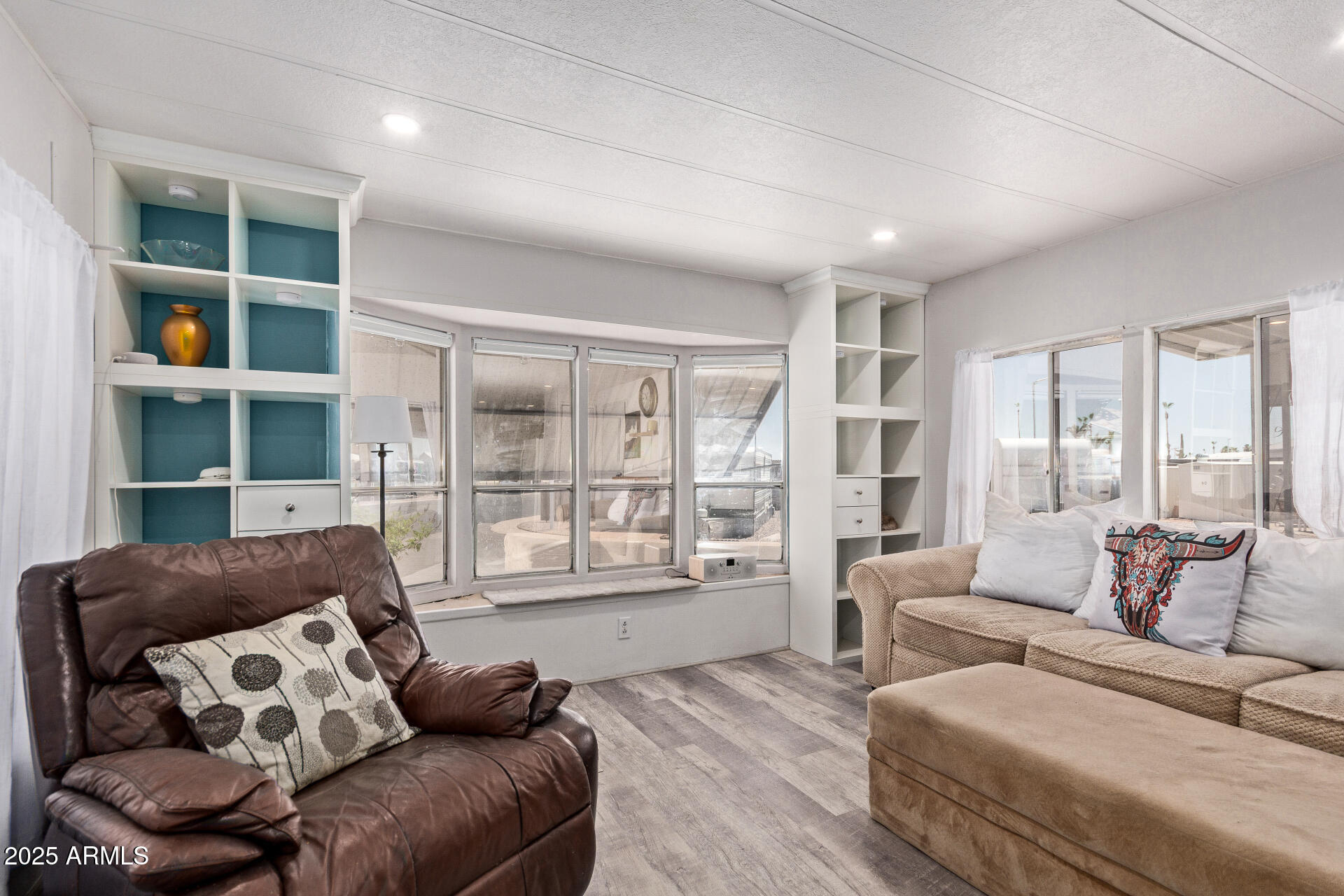 Living room with leather and beige seating, teal-backed built-ins, and large windows.