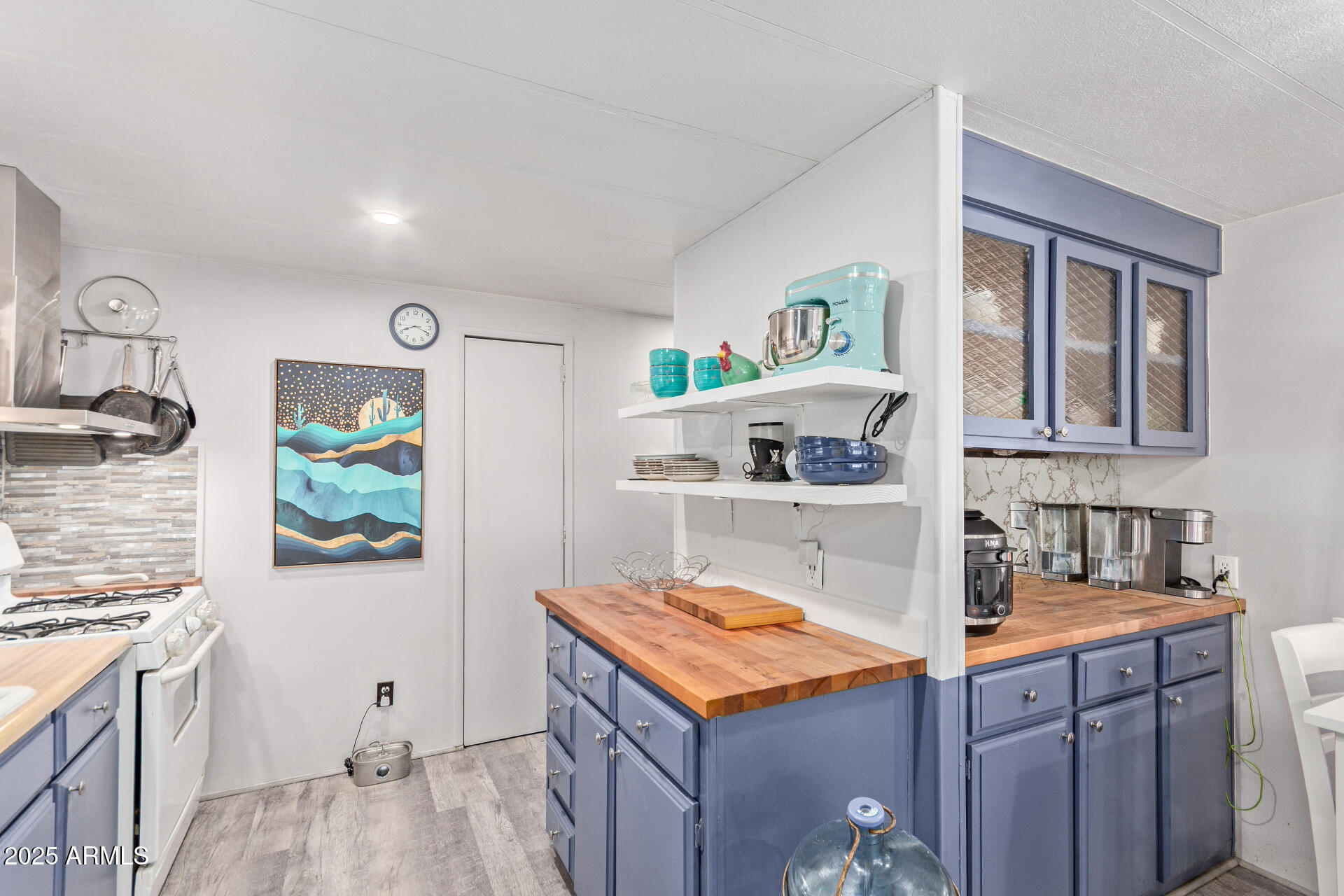 Kitchen with blue-gray cabinets, butcher-block counters, open shelves, and a turquoise stand mixer.