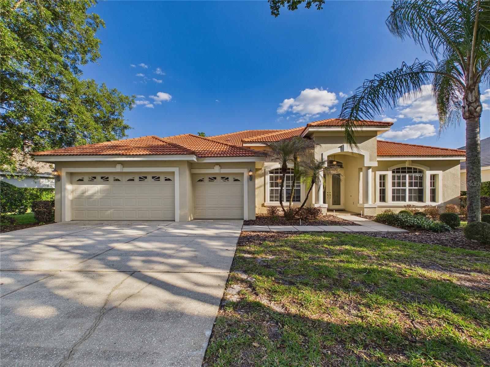 Single-story stucco home with a terracotta tile roof, two garage doors, and palm trees.