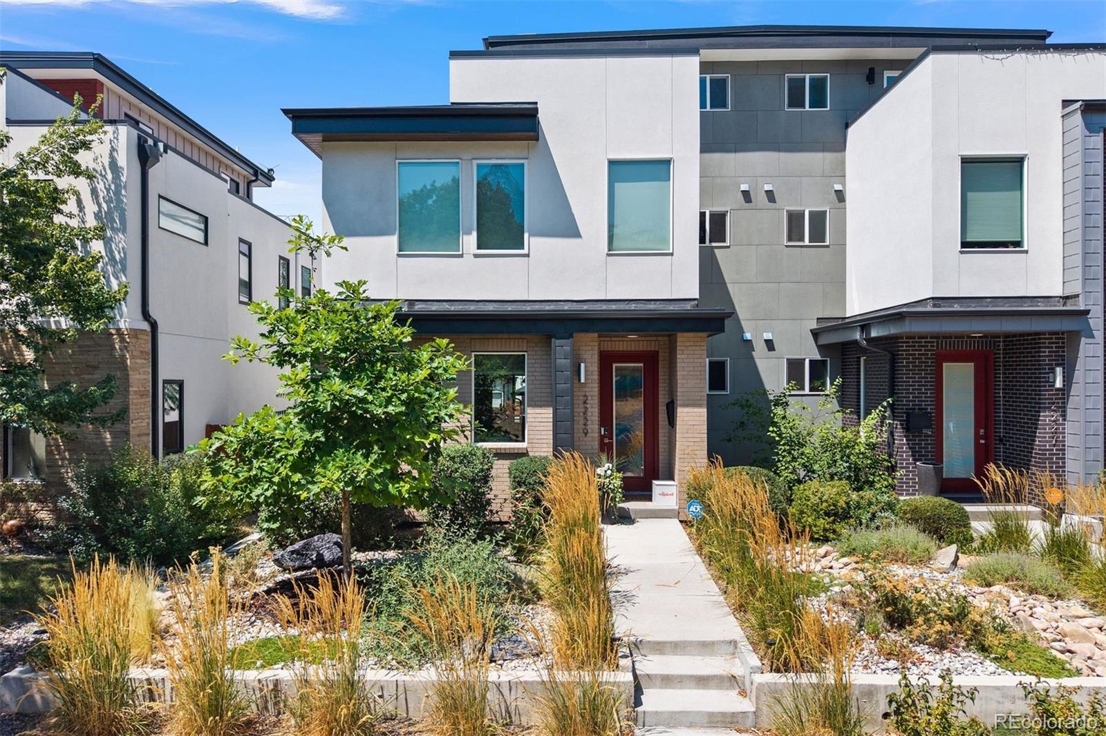 Modern attached townhomes with red entry doors and xeriscape landscaping along a central walkway.
