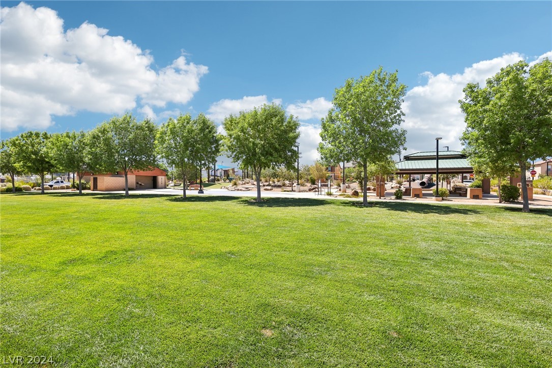 Community park with a broad green lawn, mature trees, a pavilion, and playground equipment.