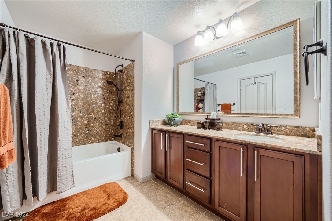 Bathroom with a pebble-tile tub surround and long dark wood vanity beneath a large mirror.