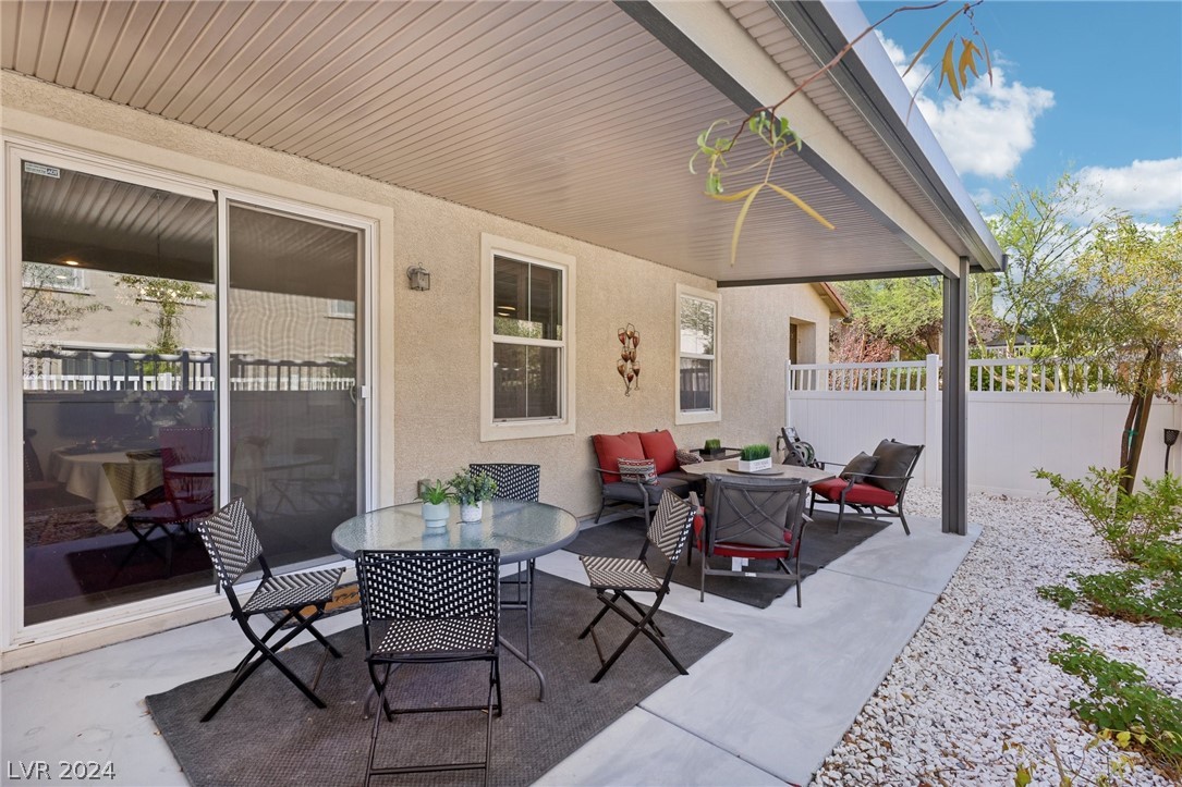 Covered backyard patio with outdoor dining and cushioned seating beside the home.