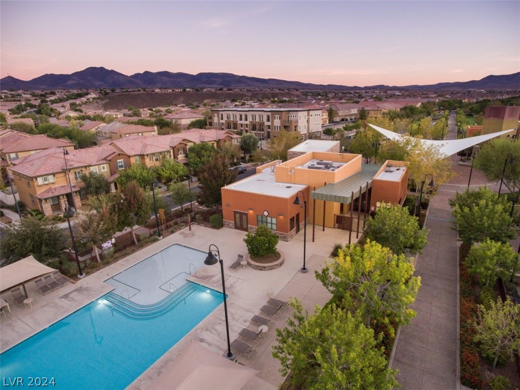 Aerial view of a community pool and recreation building among homes, with mountains at sunset.