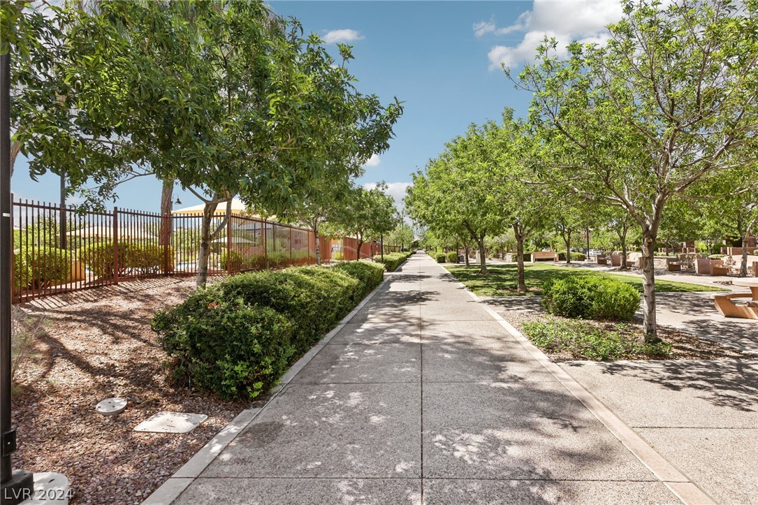 Community walkway shaded by mature trees, with benches and landscaped planting beds.