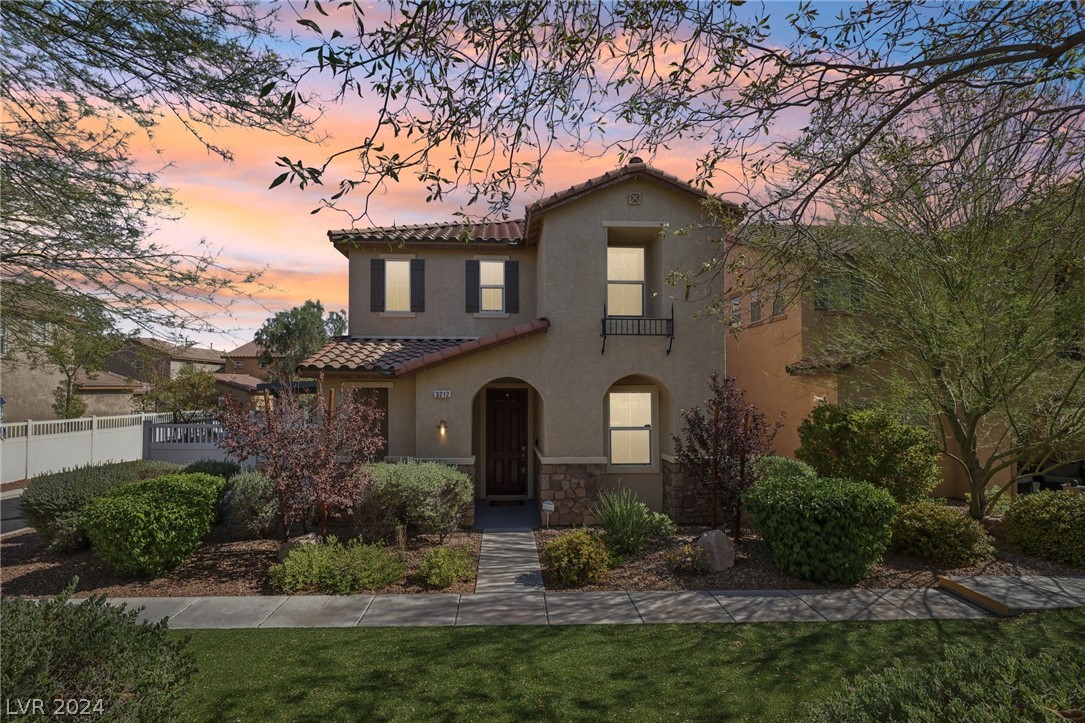 Two-story stucco home with arched entry and landscaped front yard beneath a pink sunset.