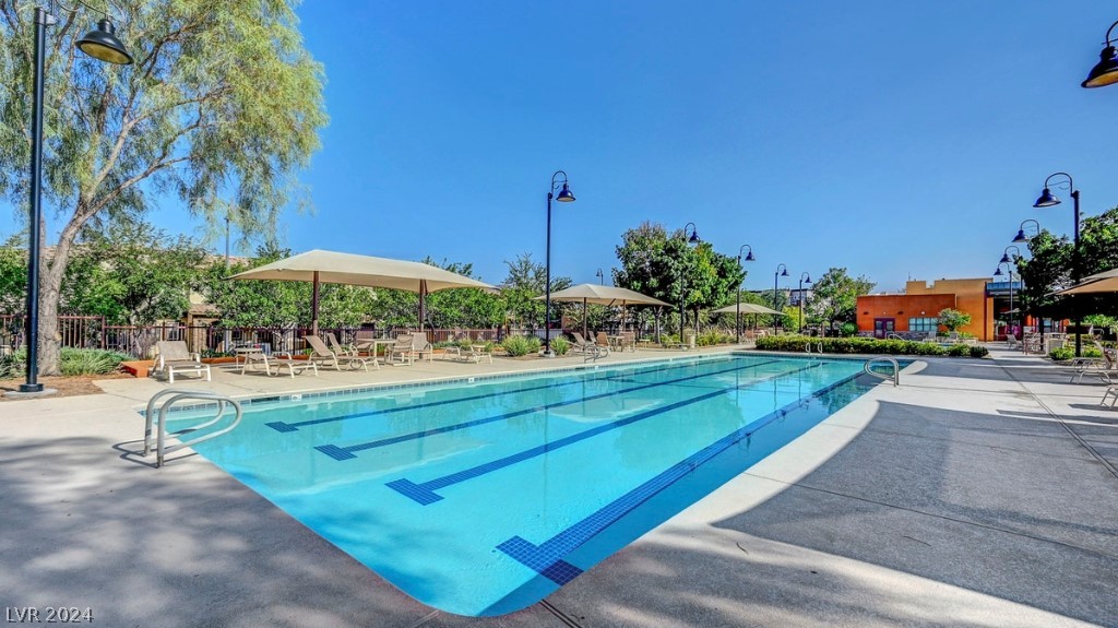 Community swimming pool with lap lanes, shaded lounge chairs, and trees.