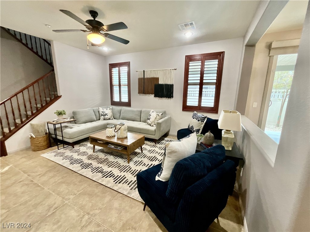Living room with a light sectional, navy armchairs, tiled floors, and a wood-railed staircase.