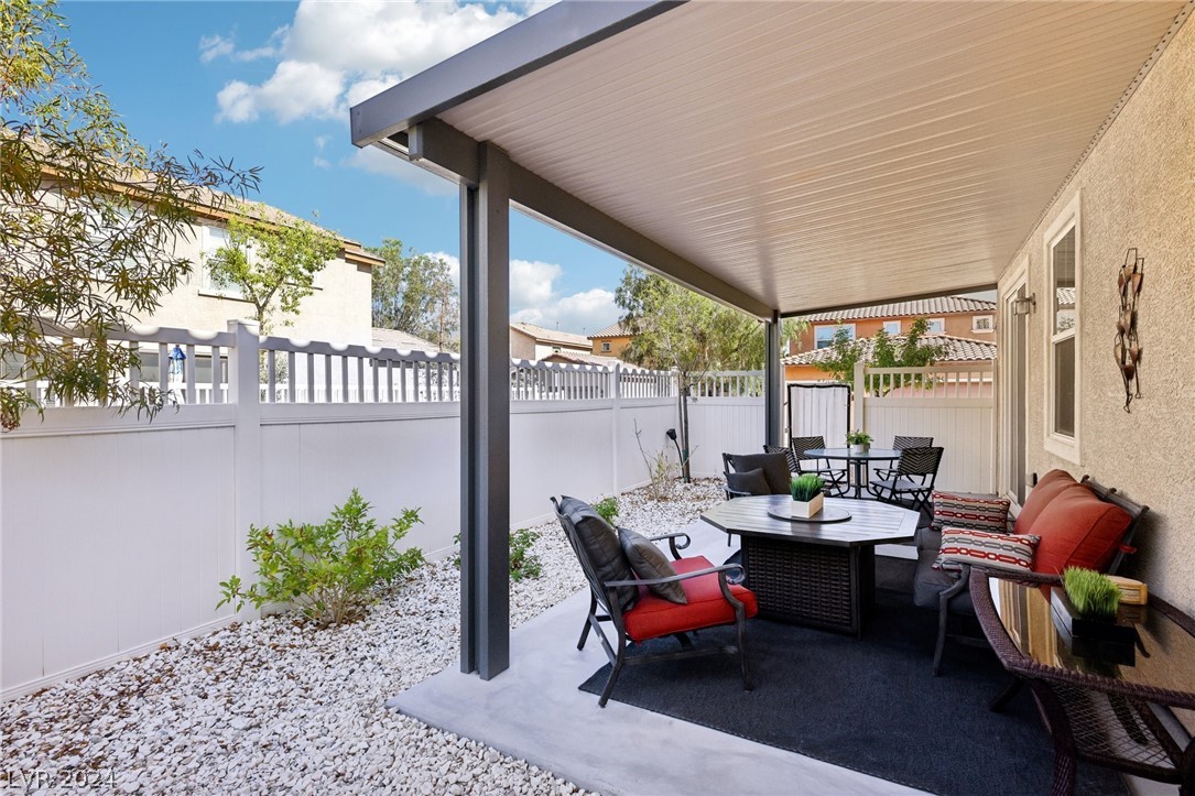 Covered backyard patio with red-cushioned lounge seating, dining furniture, and gravel landscaping.