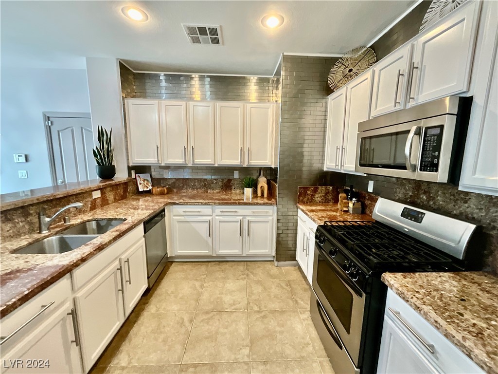 Kitchen with white cabinetry, granite countertops, stainless appliances, and a tiled backsplash.
