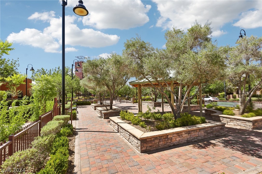 Community courtyard with brick paths, raised planters, mature trees, and a shaded pergola.