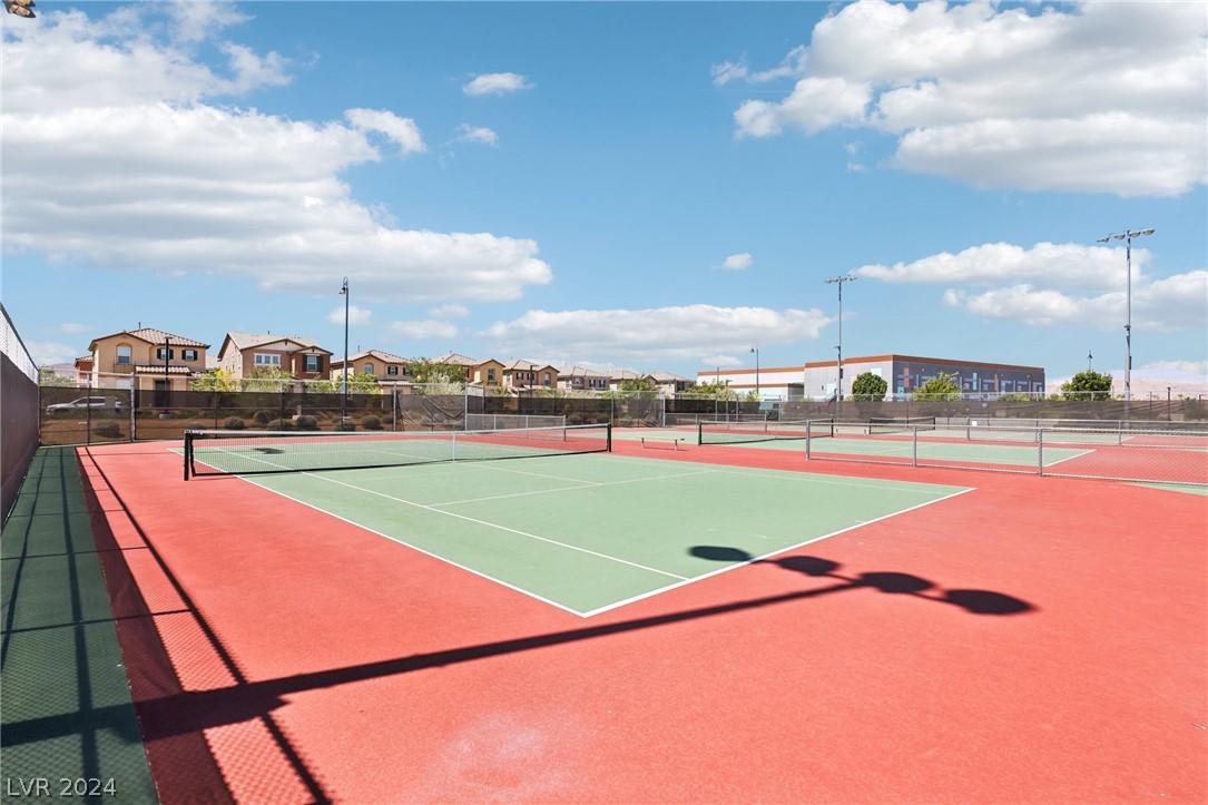 Outdoor tennis court with green and red surfaces, nets, and homes in the distance.