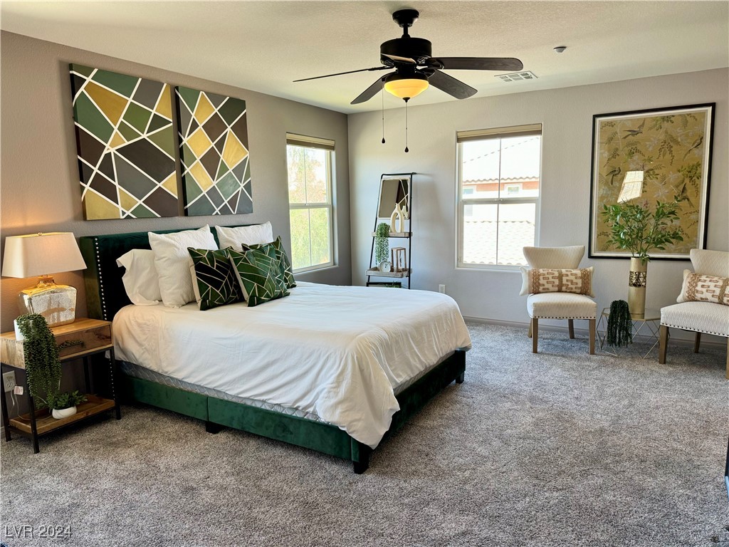 Bedroom with a green upholstered bed, geometric wall art, and a sitting area by two windows.