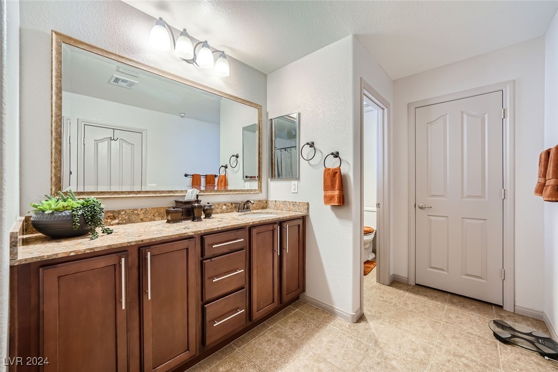 Bathroom with dark wood vanity, stone countertop, large mirror, and orange towels.