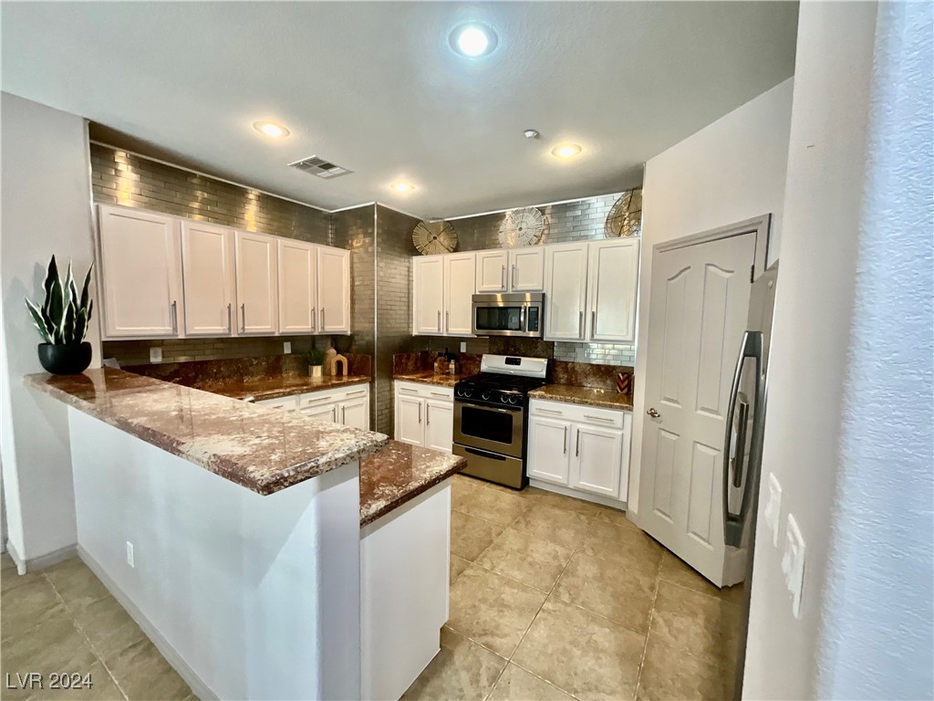 Kitchen with white cabinets, brown granite counters, stainless steel appliances, and a peninsula bar.