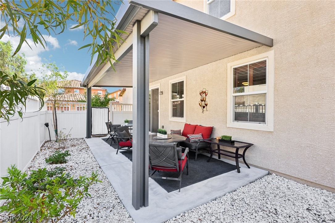 Covered backyard patio with red-cushioned seating, a dining set, white gravel, and privacy fencing.