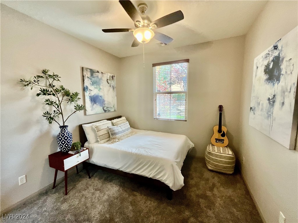 Furnished bedroom with a white bed, abstract art, and a guitar beside a striped ottoman.