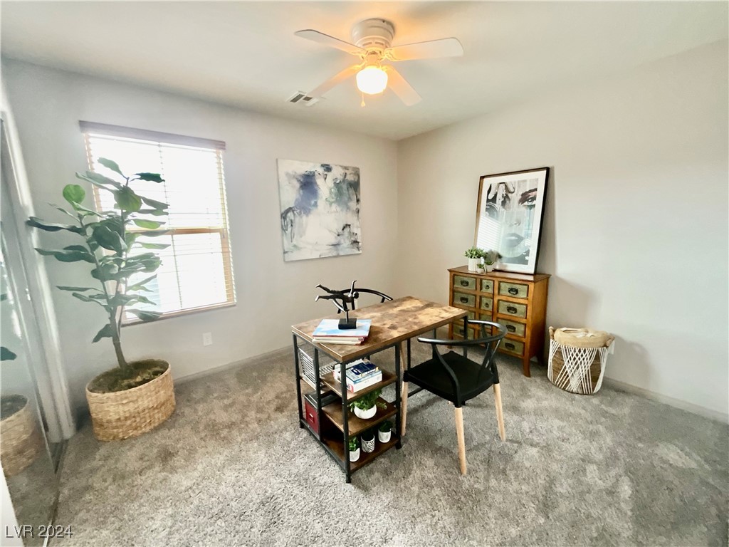 Furnished home office with a wood-and-metal desk, black chairs, and a tall potted plant by the window.